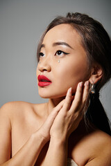 portrait of elegant asian woman with red lips folding hands and looking to up on grey background