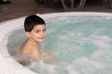 Boy sitting in the warm bubbling water jacuzzi. Happy kid relaxing in spa