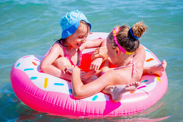 Portrait of two beautiful fun cool girls having fun in the sea on an inflatable circle. Summer holiday, rest, vacation, people, joy, happiness concept.