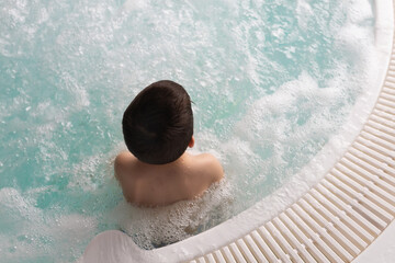 Boy sitting in the warm bubbling water jacuzzi. Happy kid relaxing in spa - 767076010