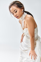 charming asian girl in elegant  white dress leaning forward and looking to down on light background