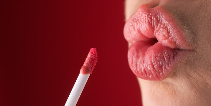 Girl puts lipstick on lips with a brush. Close-up of womens lips with lipstick. Applying lipstick on a lip. Professional lipstick.