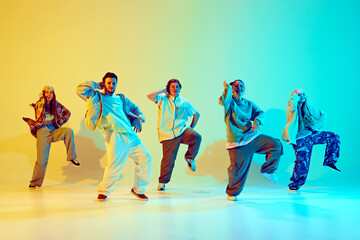 Five dancers, men and women in vibrant casual clothes striking dynamic poses over gradient green yellow background in neon light. Concept of modern dance style, hobby, active lifestyle, youth culture
