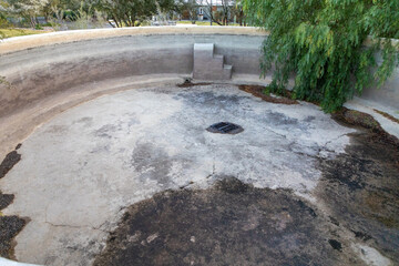 Part of an empty large round concrete pool.  At the bottom of the pool there are cracks.  Concept for leaking pools. 