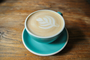 Warm coffee /cappuccino in green cup with latte art on wooden table.