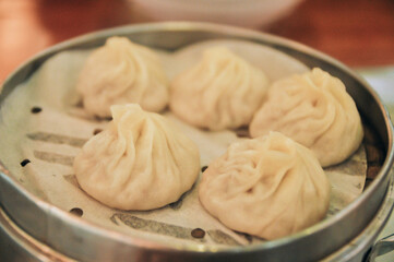 Closeup of Steamed Chinese Xiao Long Tang Bao, also known as soup dumplings because the filling inside is actually liquid soup served brown wooden streamer on wood table in the Asian restaurant