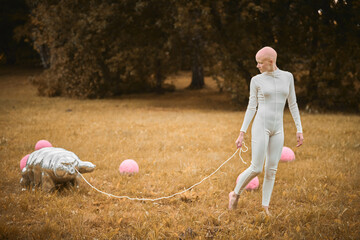 Portrait of young hairless girl with alopecia in white cloth walking tardigrade toy in fall park,...