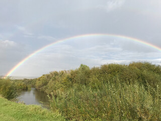 Double rainbow over an overgrown plain river after rain.