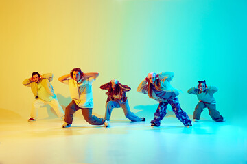 Dynamic performance of five talented dancers in motion, dancing modern dance over gradient green yellow background in neon light. Concept of modern dance style, hobby, active lifestyle, youth culture