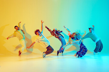 Dynamic performance of five talented dancers in motion, dancing modern dance over gradient green yellow background in neon light. Concept of modern dance style, hobby, active lifestyle, youth culture