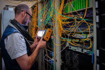 A man measures the optical signal level in a server room. A technician repairs faults in a fiber...