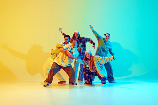 Diverse people, dancers in colorful casual clothes, standing in dynamic jumping pose, performing over gradient green yellow background in neon. Concept of modern dance style, active lifestyle, youth