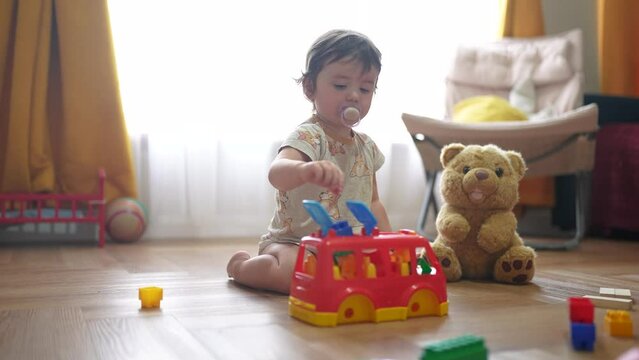 baby plays with toy bear a toy bus and puts wooden sticks in the hatch. development of fine motor skills concept. baby learns to put sticks toys into a bus car indoors in dream kindergarten