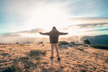Man on top of mountain spreads his arms and takes in the sunrise in cold windy winter day