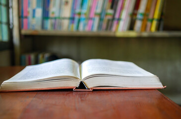 An open book or textbook vintage style on wooden table in the library and the bookshelves background.Education learning concept