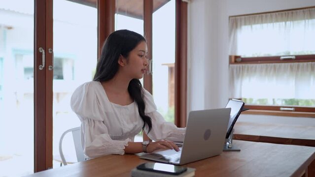 An Asian young businesswoman is working at a nearby café, using her laptop with focus and determination