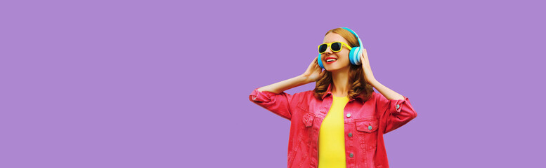 stylish modern happy young woman listening to music with headphones on purple studio background