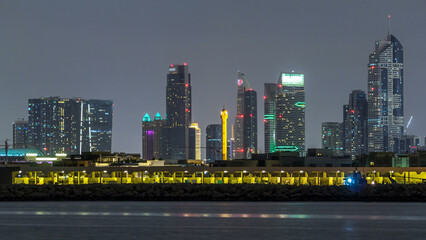 Modern Dubai city skyline timelapse at night with illuminated skyscrapers over water surface