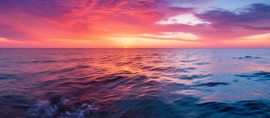 Fototapeta premium As dusk falls, the sunset paints the sky over the ocean in shades of purple, creating a stunning natural landscape. Clouds reflect in the water, adding to the serene atmosphere of the afterglow