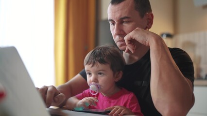 father working from home a remotely with baby fun daughter in his arms. pandemic remote work business concept. father tries to work at home in kitchen, baby children interfere sitting on their hands - 767105457