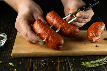 Close-up of a chef hands with meat sausages and a fork for delicious grilling. Low key barbecue...