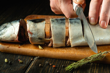Close-up of a cook hands cutting mackerel fish with a knife before frying. The concept of preparing a fish menu for lunch with spices