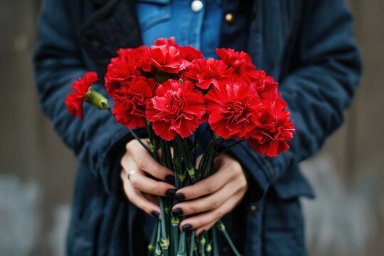 Person in a blue shirt and black coat holding a bouquet of red carnations