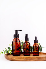 Mockup of amber glass bottles with serum, jars of hand cream, faces on wooden stand isolated on white background.