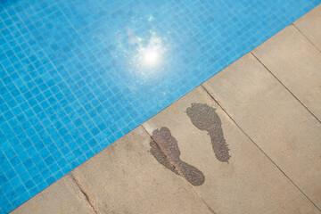 Wet footprints on pool edge, view from the top