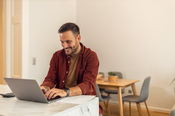 A smiling adult businessman typing on his laptop while working from home