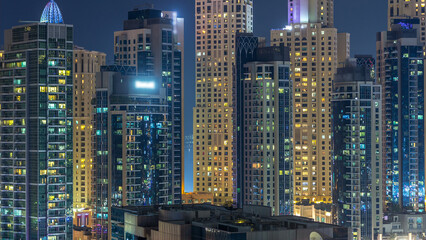 Glowing windows in multistory modern glass and metal residential buildings light up at night timelapse.