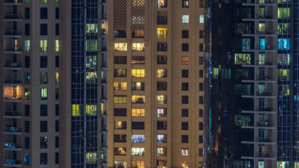 Fototapeta na wymiar Glowing windows in multistory modern glass and metal residential building light up at night timelapse.