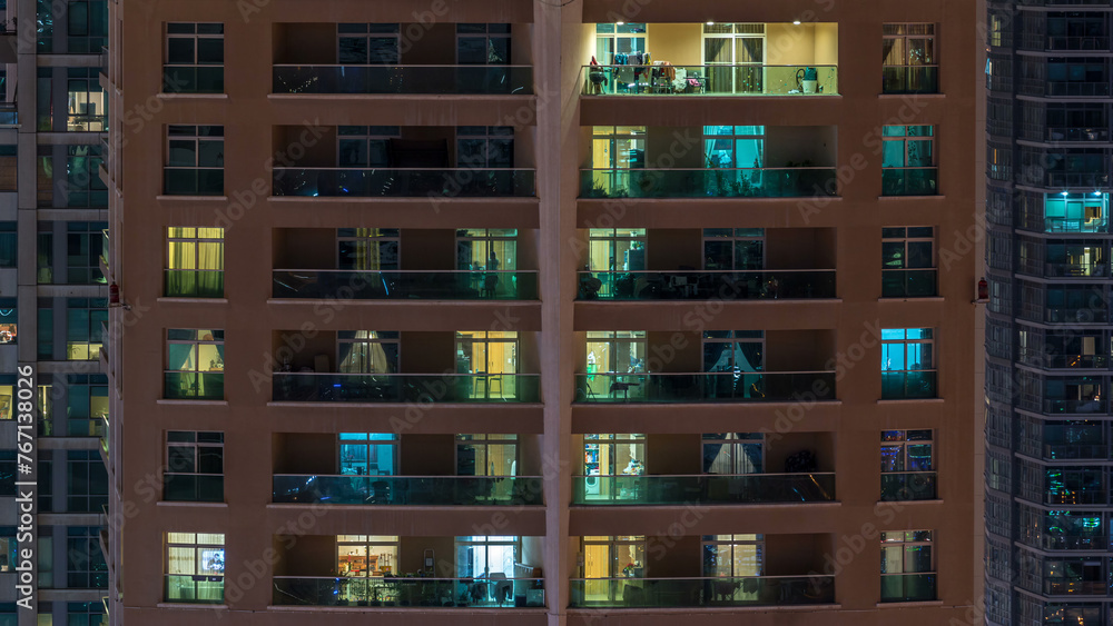 Wall mural Glowing windows in multistory modern glass residential building light up at night timelapse.