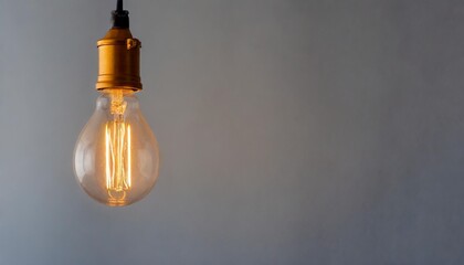 a vintage light bulb hanging from a ceiling glowing warmly against a cool grey background with copy space