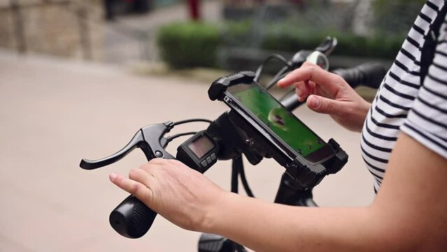 Close-up woman using mobile phone with green chromakey mockup touch screen, renting an electric bike using a rental app on mobile phone. Bike sharing city service. Sustainability. Public eco transport