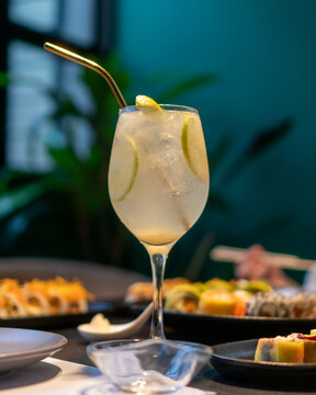 A cup of Gin and Tonic with lemon slices on a black gourmet sushi table of a delicate restaurant with a plant in the background