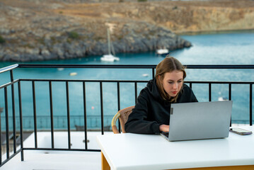 A young girl uses a laptop on the balcony at sunset. - 767149833