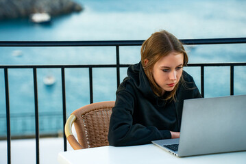 A young girl uses a laptop on the balcony at sunset. - 767149836