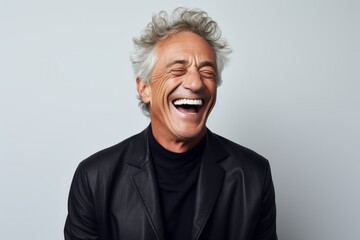 Handsome mature man laughing and looking at camera while standing against grey background