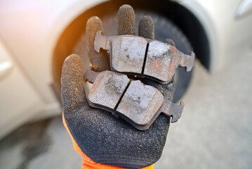 Mechanic holds bad brake pads in hand, replacing worn uneven defective pads. Vehicle brake system...