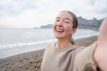 Self portrait of attractive smiling young woman spending sunny day weekend at the beach, carefree girl makes selfie poses against sea or ocean, outside shot