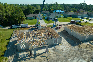 Professional builders and crane truck working on roof construction of unfinished suburban home with...