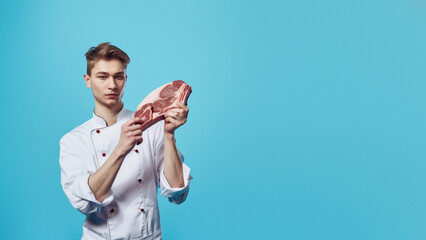 Young male chef in white uniform closely examines a cut of raw steak, focusing on quality