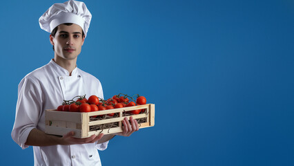 A focused young chef in formal white attire holding a crate of tomatoes