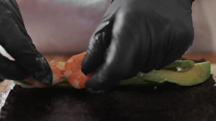Chef in black gloves carefully crafts sushi rolls, expertly combining rice, avocado, and shrimp. Concept of culinary mastery and harmonious blend of ingredients in sushi cuisine.