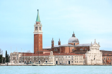 Fototapeta premium Beautiful landscape of the Church of San Giorgio Maggiore with boats docked outside, seen across the Venetian lagoon, beneath light blue sky - Venice, Italy