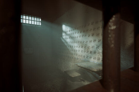 Dim prison cell with tally marks on concrete wall and barred window