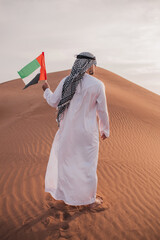Arab man holding UAE flag walking in the desert ,national day celebration - spirit of the union 
