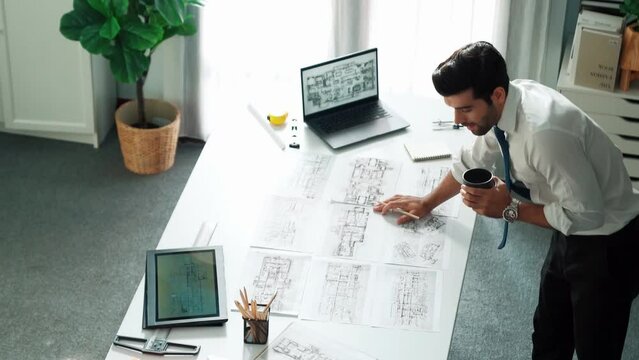 Architect engineer using laptop planning house design at office while sitting at meeting table with blueprint and equipment scatter around.Skilled civil engineer working at blueprint. Alimentation.