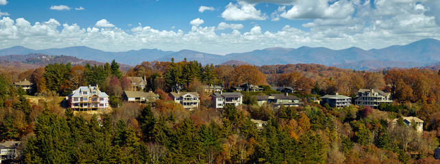 Fototapeta na wymiar Aerial view of big family houses on mountain top between yellow trees in North Carolina suburban area in fall season. Real estate development in american suburbs